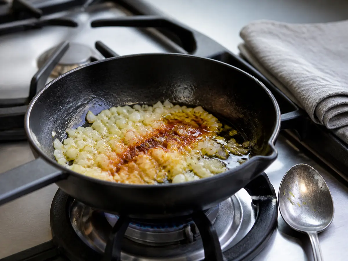 Small skillet with onion and a pinch of reddish-brown spice blooming in oil - baharat substitute pan test | KnowTheSpices
