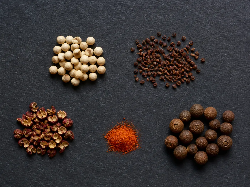 White peppercorns, grains of paradise, Sichuan peppercorns, cayenne, and allspice in measured portions - black pepper substitutes | KnowTheSpices