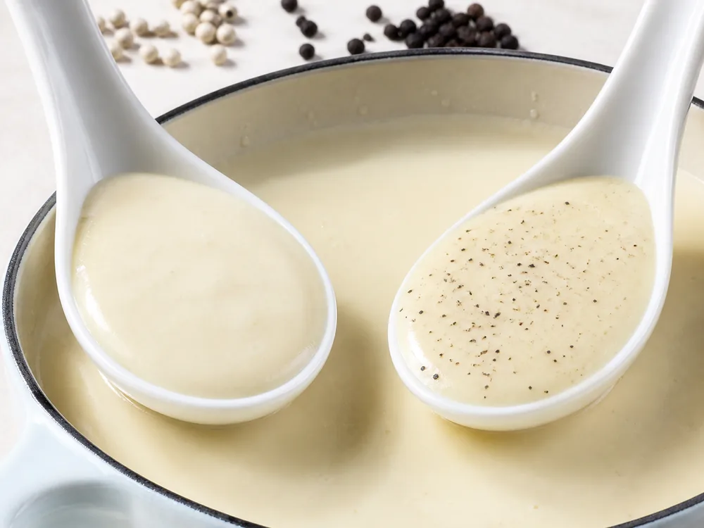 White pepper and black pepper compared in two spoonfuls of pale bechamel sauce - black pepper substitute for white sauce | KnowTheSpices