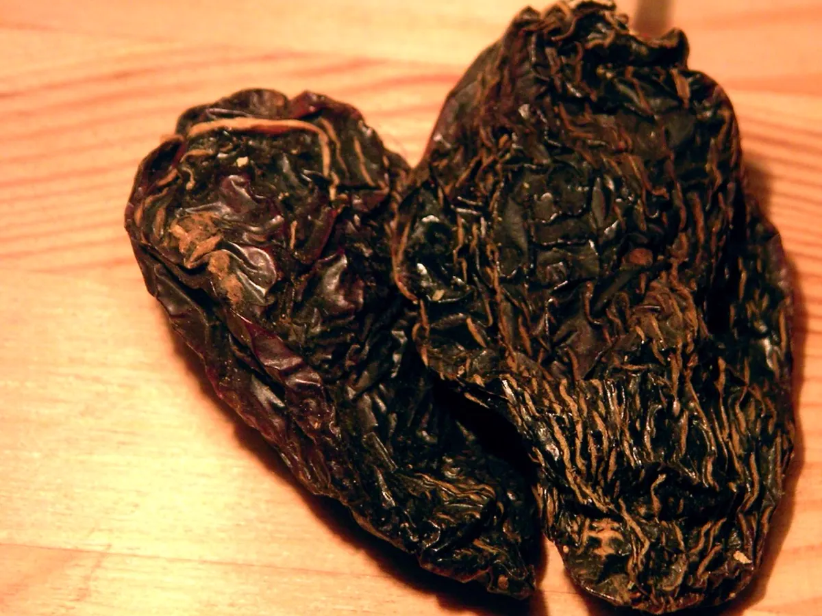 Two dark wrinkled smoke-dried chipotle peppers on a wooden surface - chipotle powder substitutes | KnowTheSpices