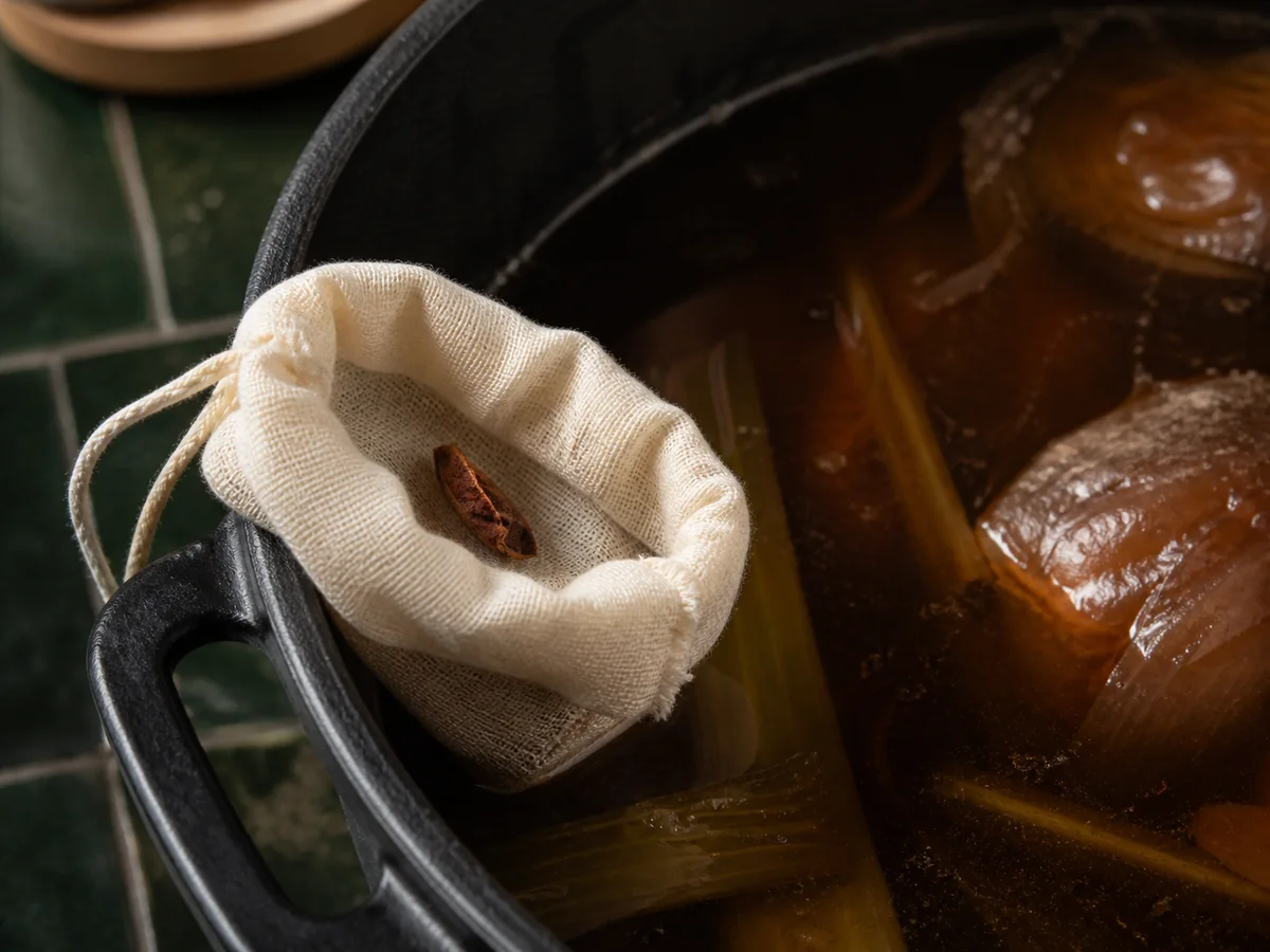 One broken star anise point in a muslin sachet beside dark stock - star anise as a clove substitute | KnowTheSpices