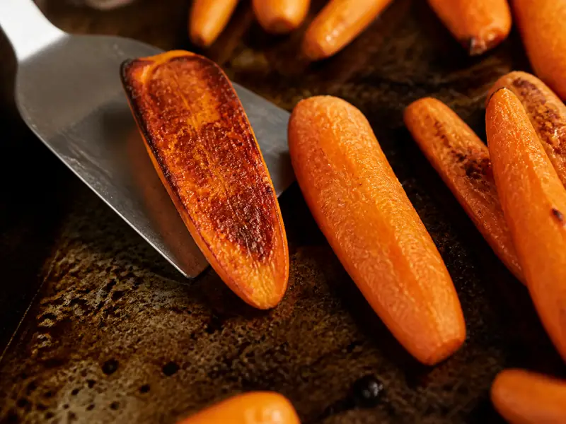 Deeply browned carrot cut face lifted beside a pale early-turned carrot on a hot tray - roasted carrot char cue | KnowTheSpices