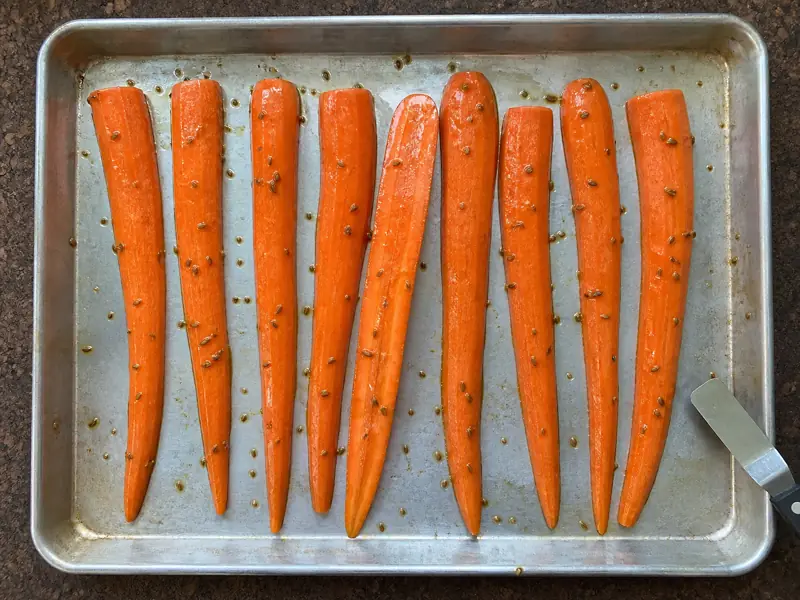 Evenly halved carrots arranged cut-side down with open space on a silver sheet pan - cumin roasted carrots | KnowTheSpices