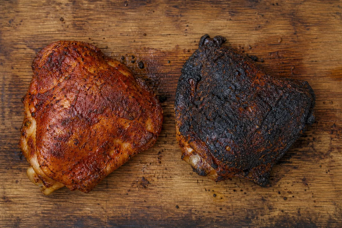 Two paprika-rubbed chicken thighs side by side, one still deep red from the cooler side of the grill and one browned and blackened from over the coals - paprika scorching on a grill | KnowTheSpices
