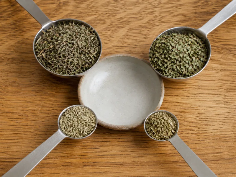 Unequal thyme, savory, rosemary, and oregano measures around a mixing bowl - herbs de Provence substitutes | KnowTheSpices
