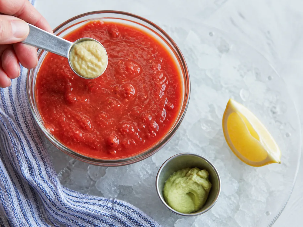 Prepared mustard measured into tomato cocktail sauce with lemon held aside - horseradish substitute for cocktail sauce | KnowTheSpices