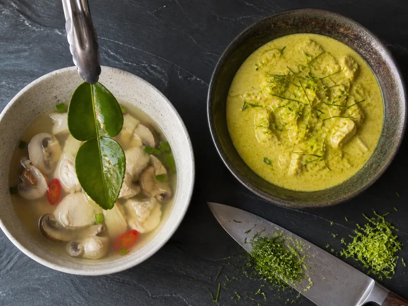 A whole aromatic being lifted from clear soup beside fine green shreds on thick curry
