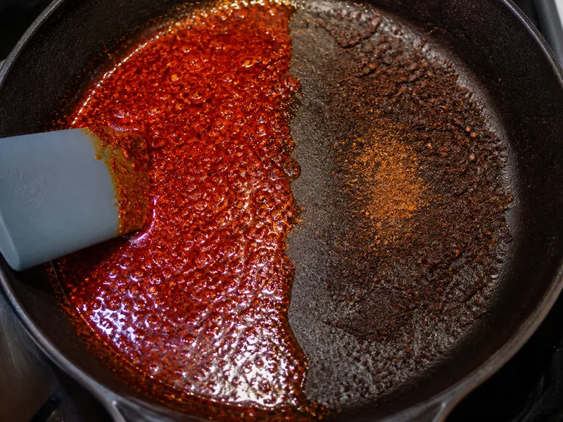 Glossy red chile powder blooming in oil beside a scorched brown patch in a skillet - Kashmiri chili powder substitutes | KnowTheSpices