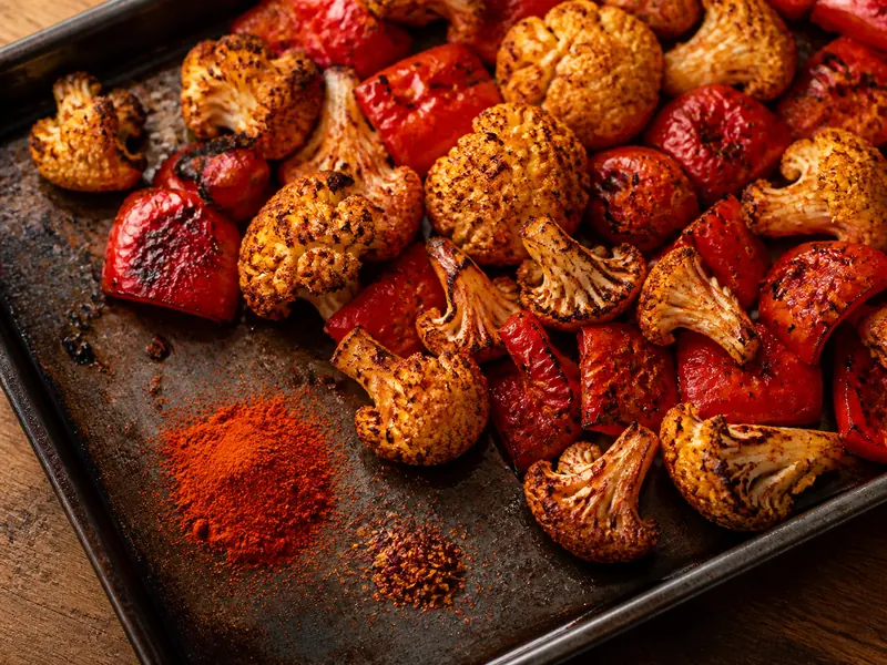 Smoked paprika and cayenne beside charred cauliflower and peppers on a roasting tray - Kashmiri chili powder substitutes | KnowTheSpices