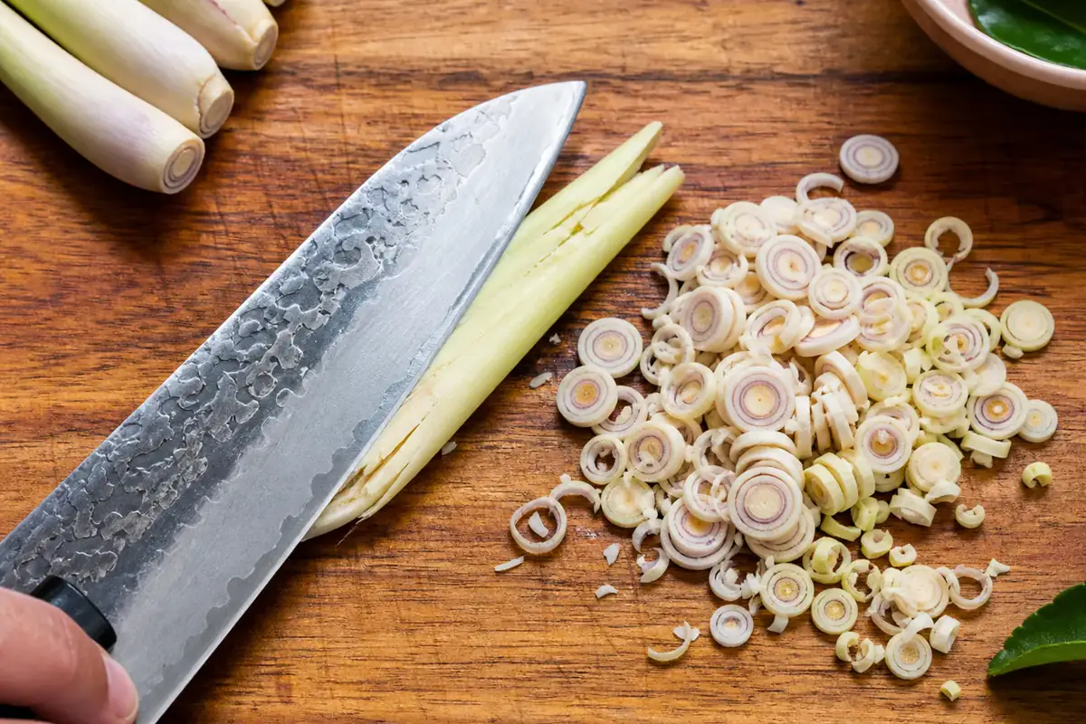 Bruised lemongrass lengths beside thin crosswise rings and a fine mince on a wooden cutting board
