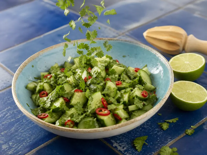 Chopped cilantro falling into a lime-dressed cucumber and chile salad