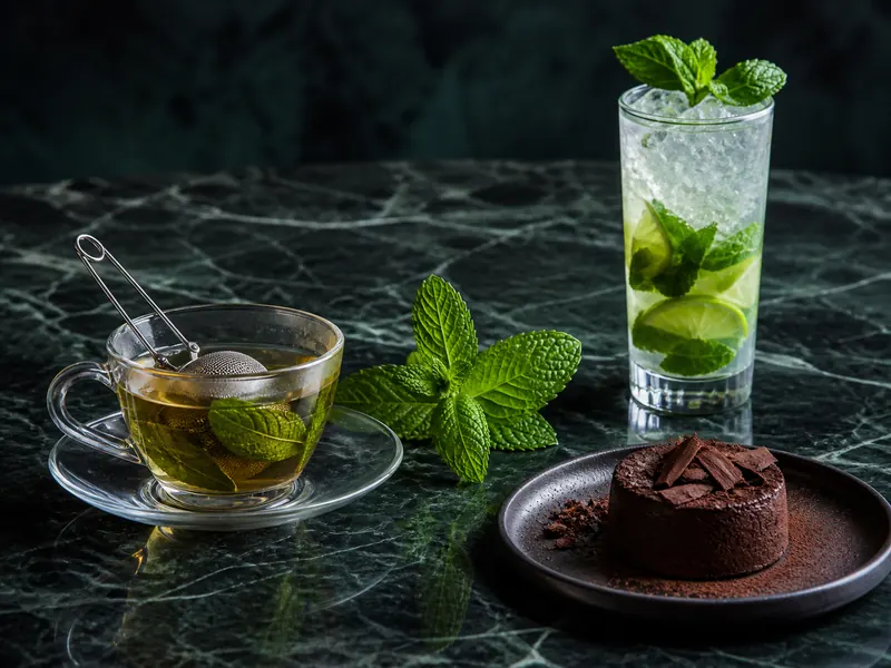 Mint tea, a lime highball, and chocolate dessert arranged around one fresh mint sprig