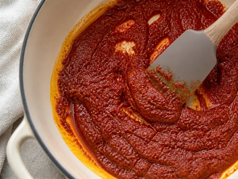 Brick-red berbere and tomato paste releasing oil at the edge of an enamel pan - misir wat spice paste | KnowTheSpices