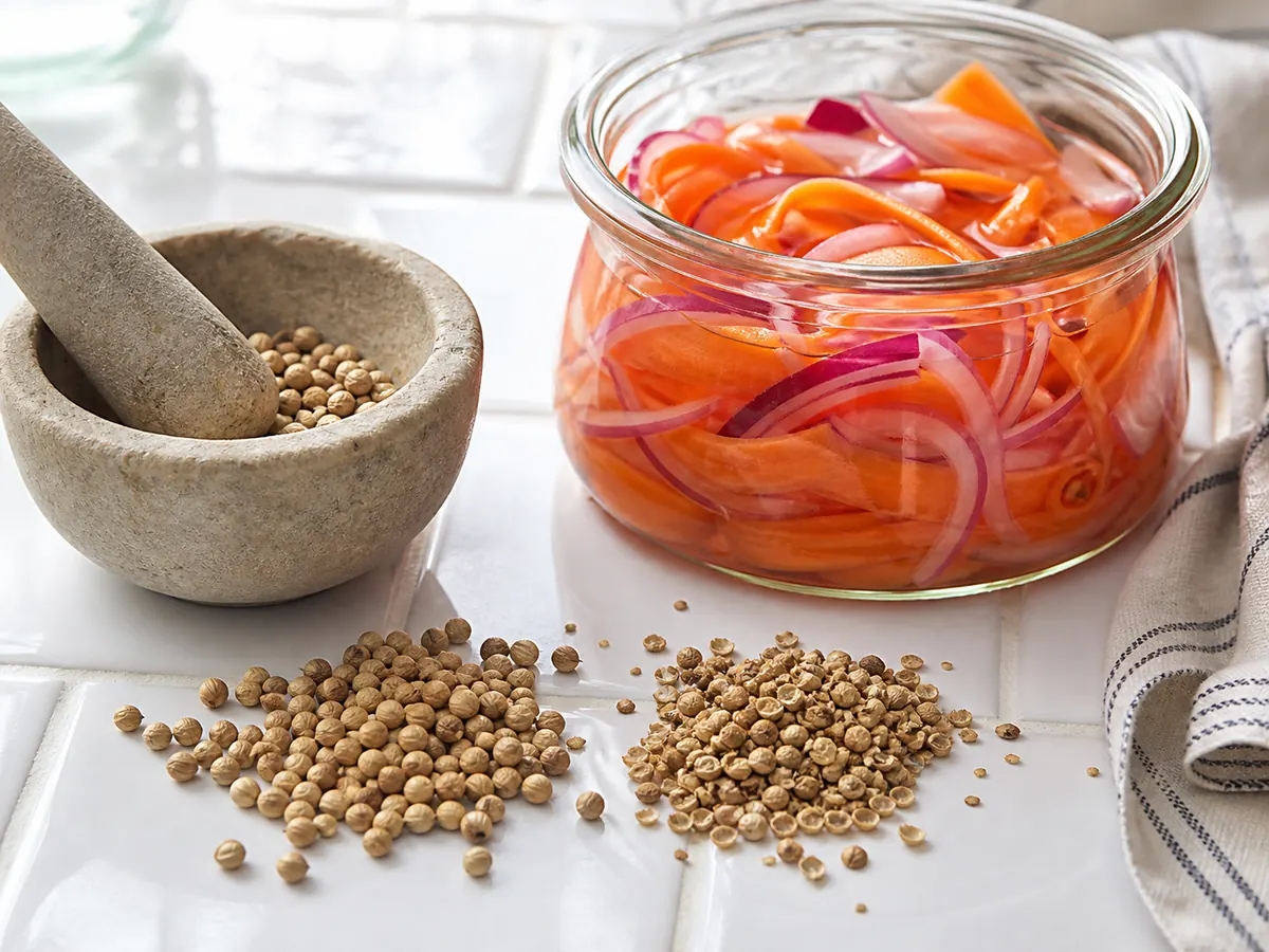 Whole and once-cracked coriander seeds beside carrot and red-onion quick pickle - mustard seed substitutes | KnowTheSpices