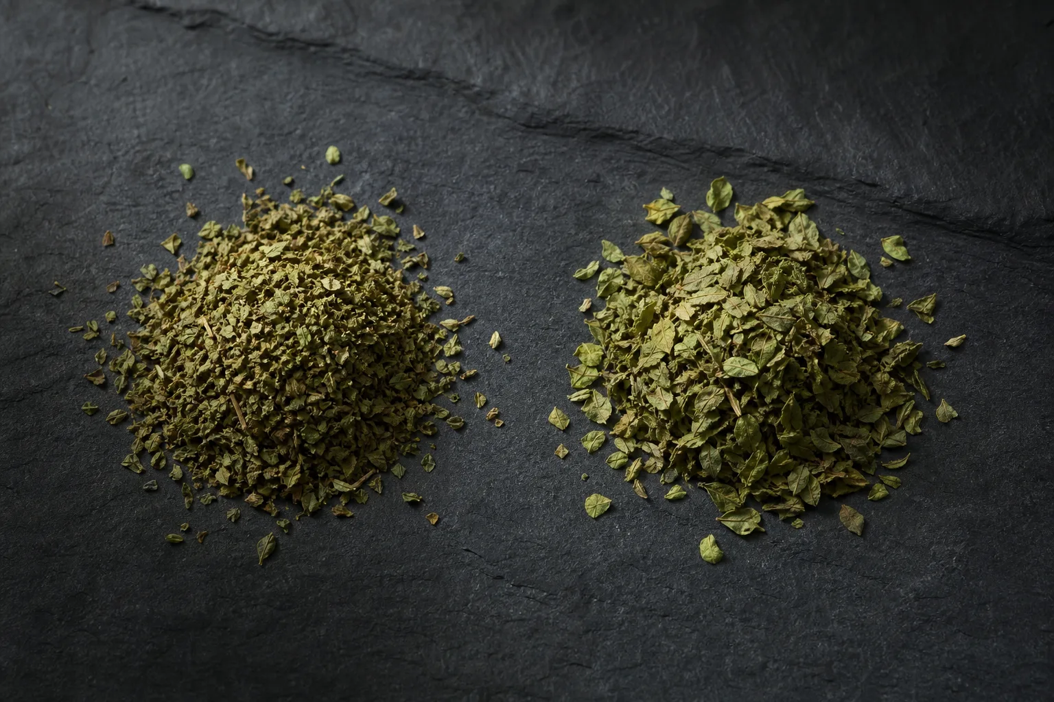 Two small piles of dried oregano labeled by leaf shape on dark slate showing Mediterranean and Mexican types