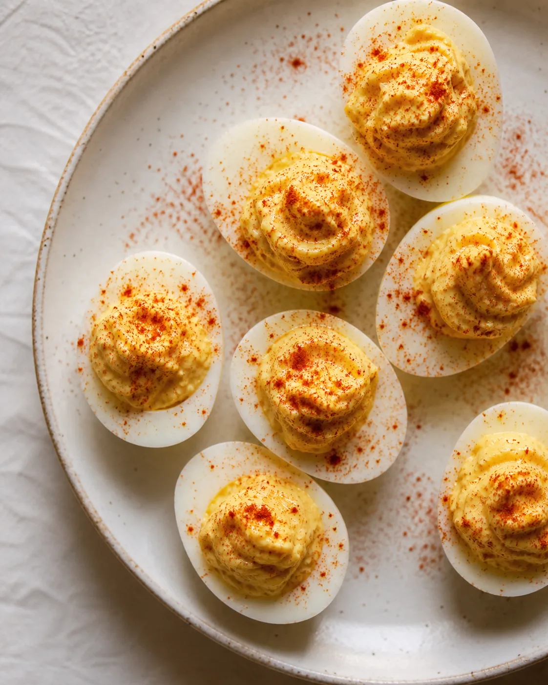 Deviled eggs on a plate finished with a light dusting of bright red sweet paprika