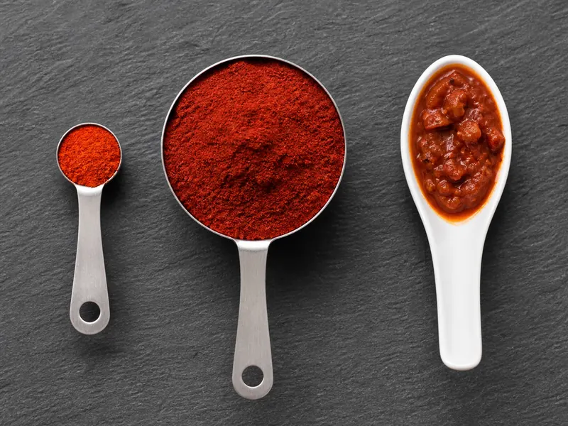 A tiny one-eighth teaspoon of cayenne beside a much larger mild red pepper measure and a stew sample