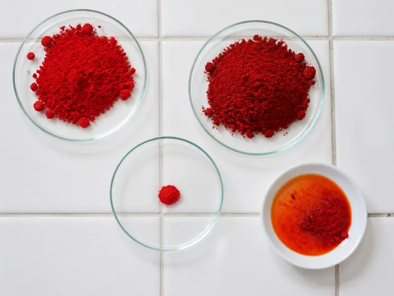 Three red pepper powders with different hues arranged around a white dish and a small red oil bloom