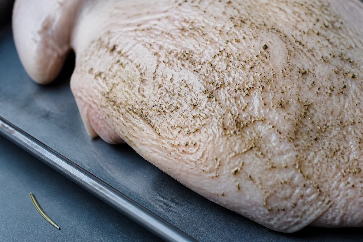 Finely crushed rosemary dispersed through oil on turkey skin beside one intact needle - poultry seasoning substitutes | KnowTheSpices