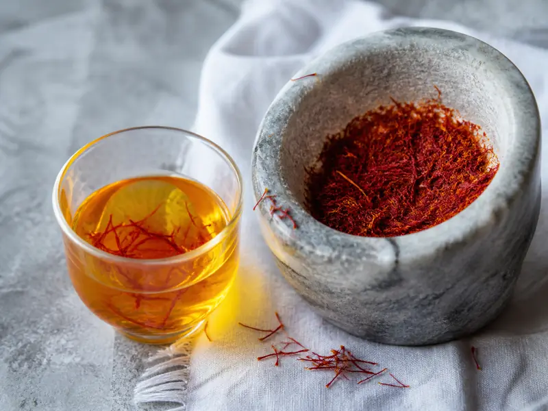 Deep-gold saffron infusion beside crushed red threads and a small stone mortar - saffron rice | KnowTheSpices