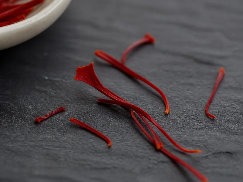 Macro view of deep crimson saffron stigmas with irregular flared tips on dark slate - saffron thread anatomy | KnowTheSpices
