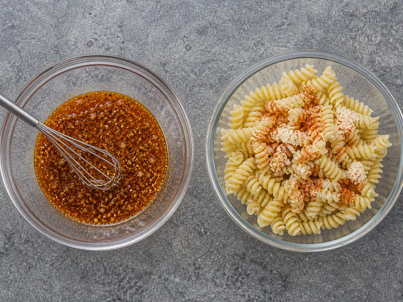 Smooth red-speckled vinaigrette beside cold pasta with dry seasoning clumps on its surface