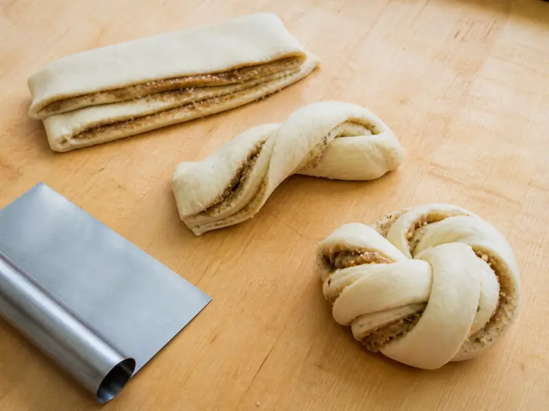 Cardamom bun dough shown as a strip, a loose twist, and a tucked knot on a maple board - shaping cardamom buns | KnowTheSpices
