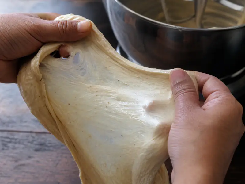 Tacky enriched cardamom dough stretched into a thin translucent windowpane above a mixer bowl - cardamom bun dough | KnowTheSpices