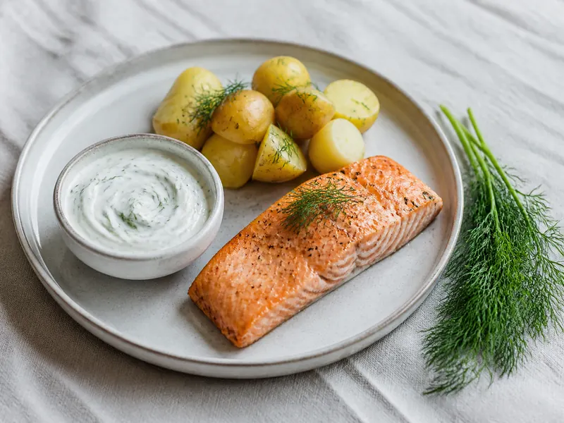 Feathery fresh dill folded into yogurt sauce beside salmon and boiled potatoes