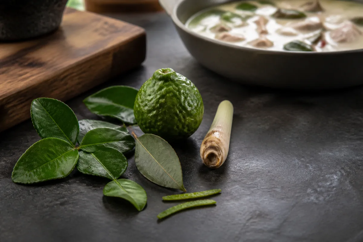 Makrut lime leaves with zest, lemongrass, and fresh bay leaf beside a coconut curry
