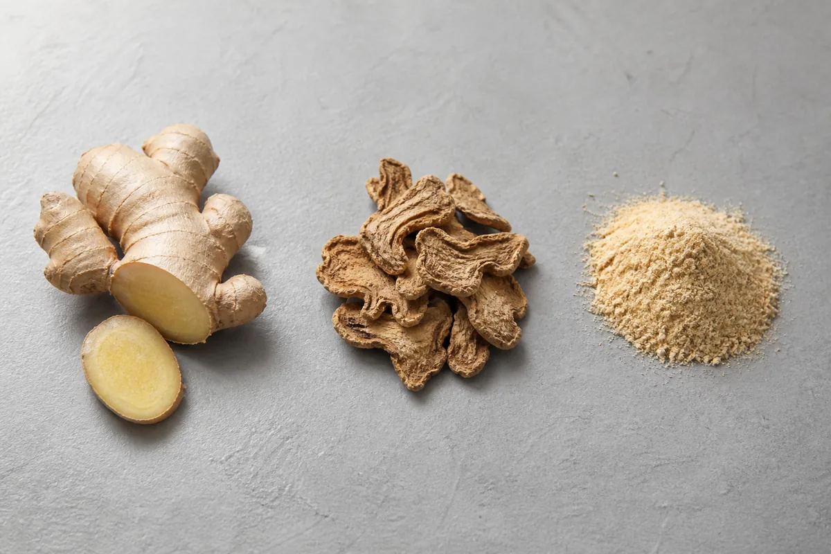 Fresh ginger root beside dried ginger slices and ground ginger powder in three separate piles - fresh and dried ginger as separate medicinals | KnowTheSpices