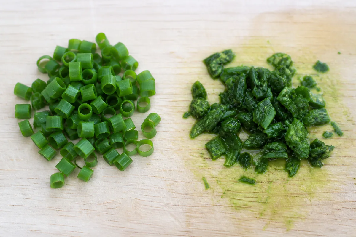 Neat crisp snipped chive rings beside a crushed bruised darkened pile with green juice on the board - snipping versus chopping chives | KnowTheSpices