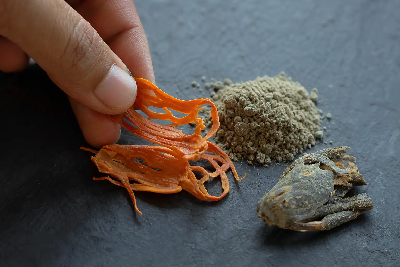 Fresh orange mace blades being broken beside dull old ground mace in an unlabeled jar